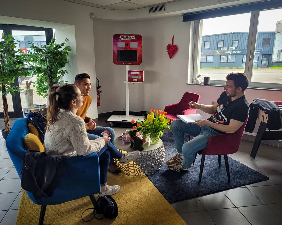 Réception en extérieur avec invités en tenue de soirée tenant des flûtes de champagne, couple au premier plan trinquant, groupe de personnes élégamment vêtues en arrière-plan sur pelouse verdoyante, lumière dorée de fin de journée