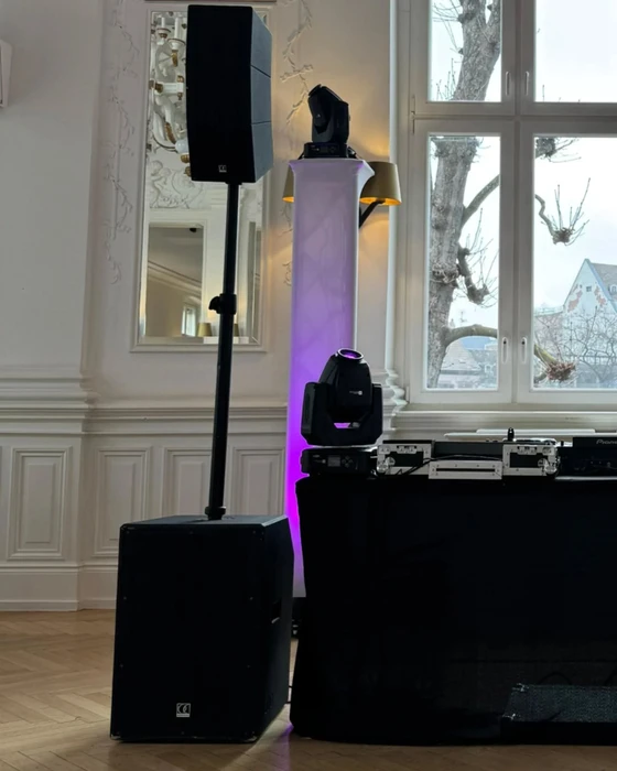 Réception en extérieur avec invités en tenue de soirée tenant des flûtes de champagne, couple au premier plan trinquant, groupe de personnes élégamment vêtues en arrière-plan sur pelouse verdoyante, lumière dorée de fin de journée